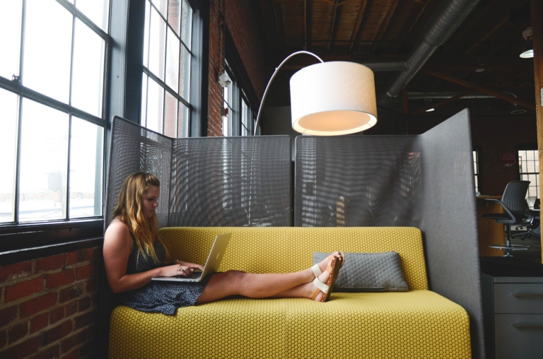 A virtual assistant works on a sofa in a co working space