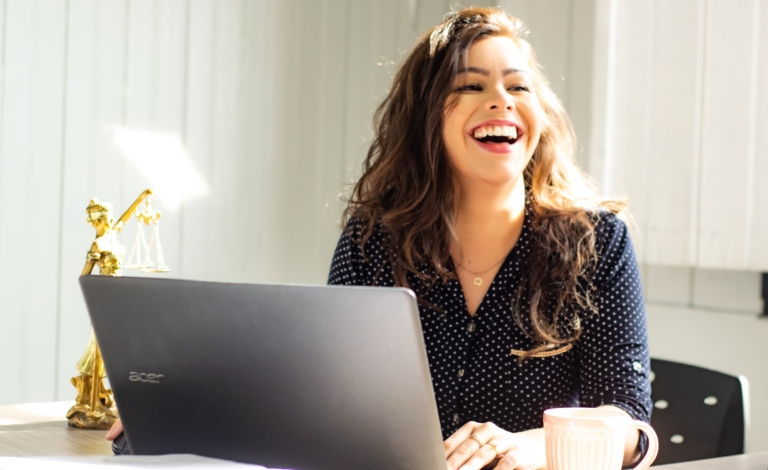 A virtual assistant smiles widely whilst working at her laptop