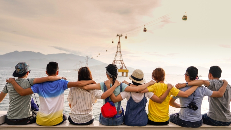 A group of 8 friends with their arms around each other look out to sea