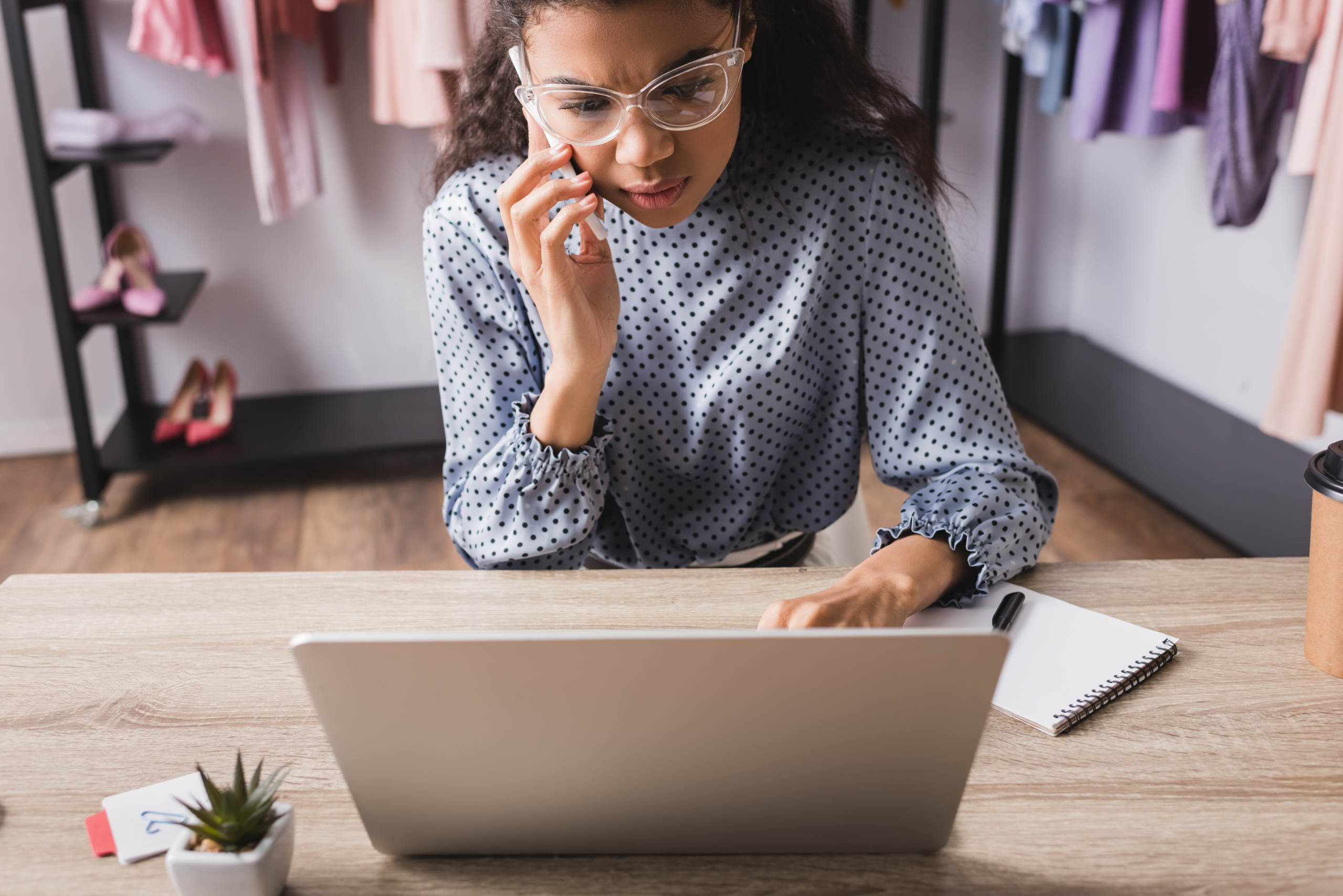 serious small business owner talking on smartphone while using laptop