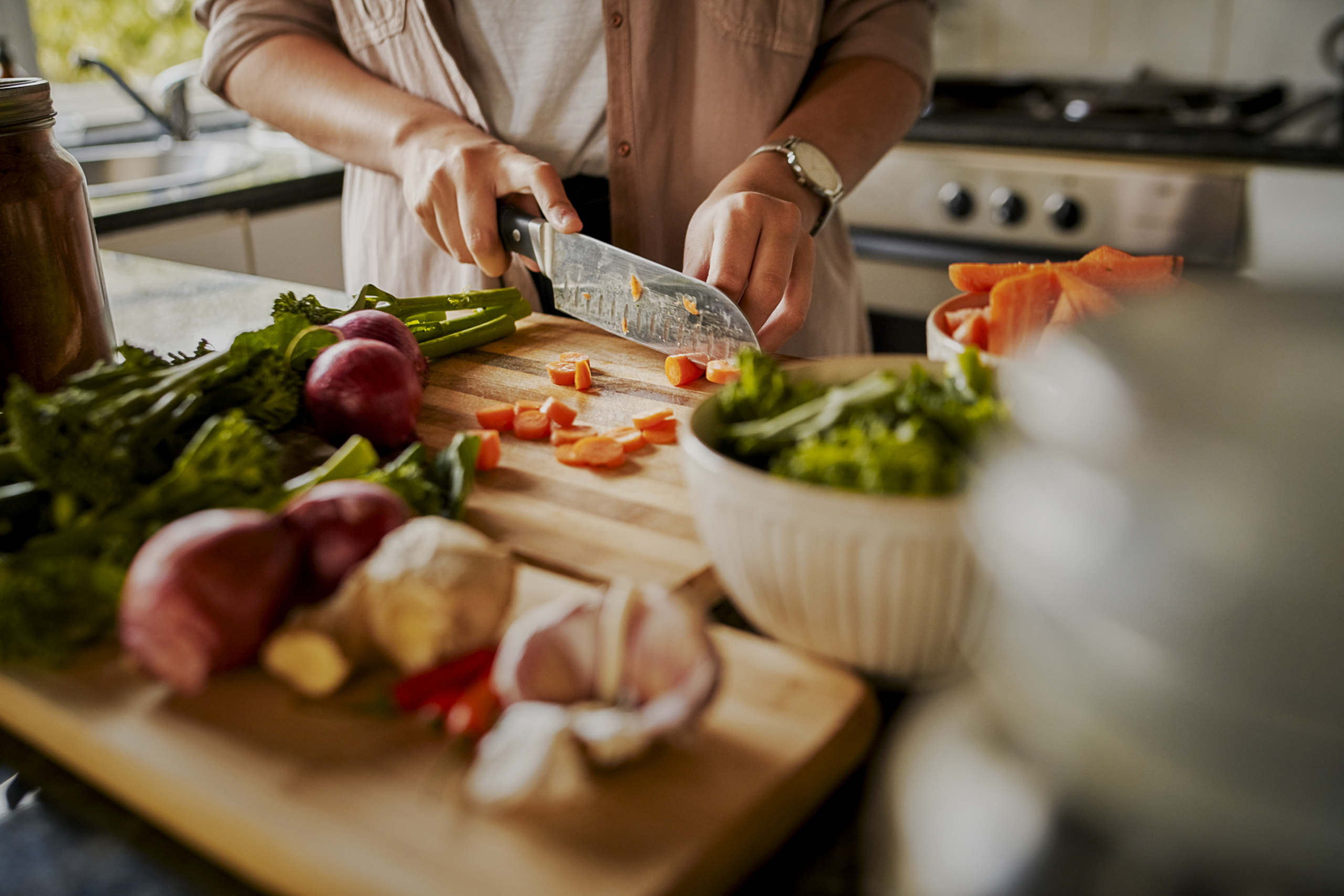 A person prepares dinner by chopping vegetables on a chopping board in a kitchen