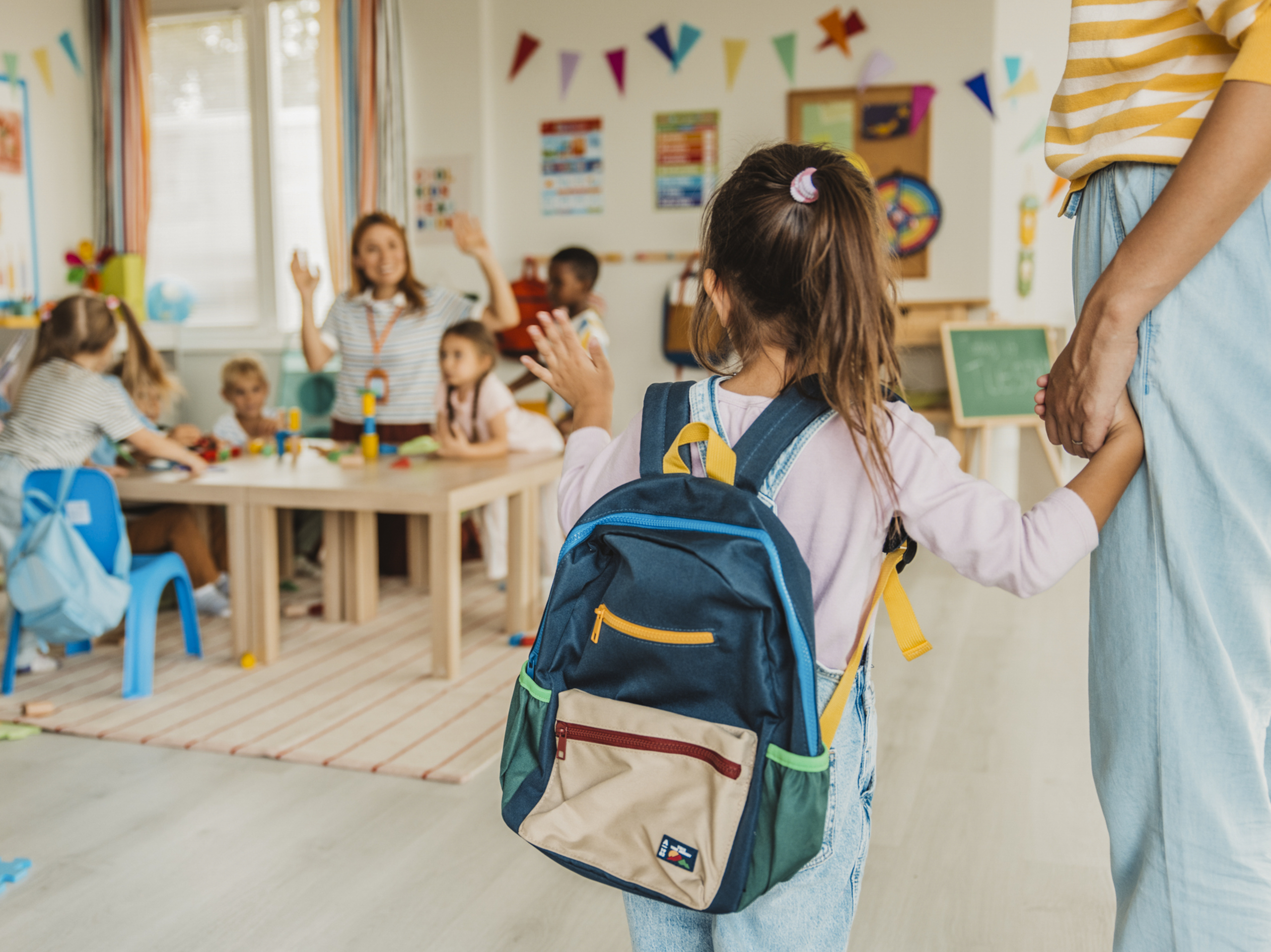 Nursery worker greets a young child and her parent