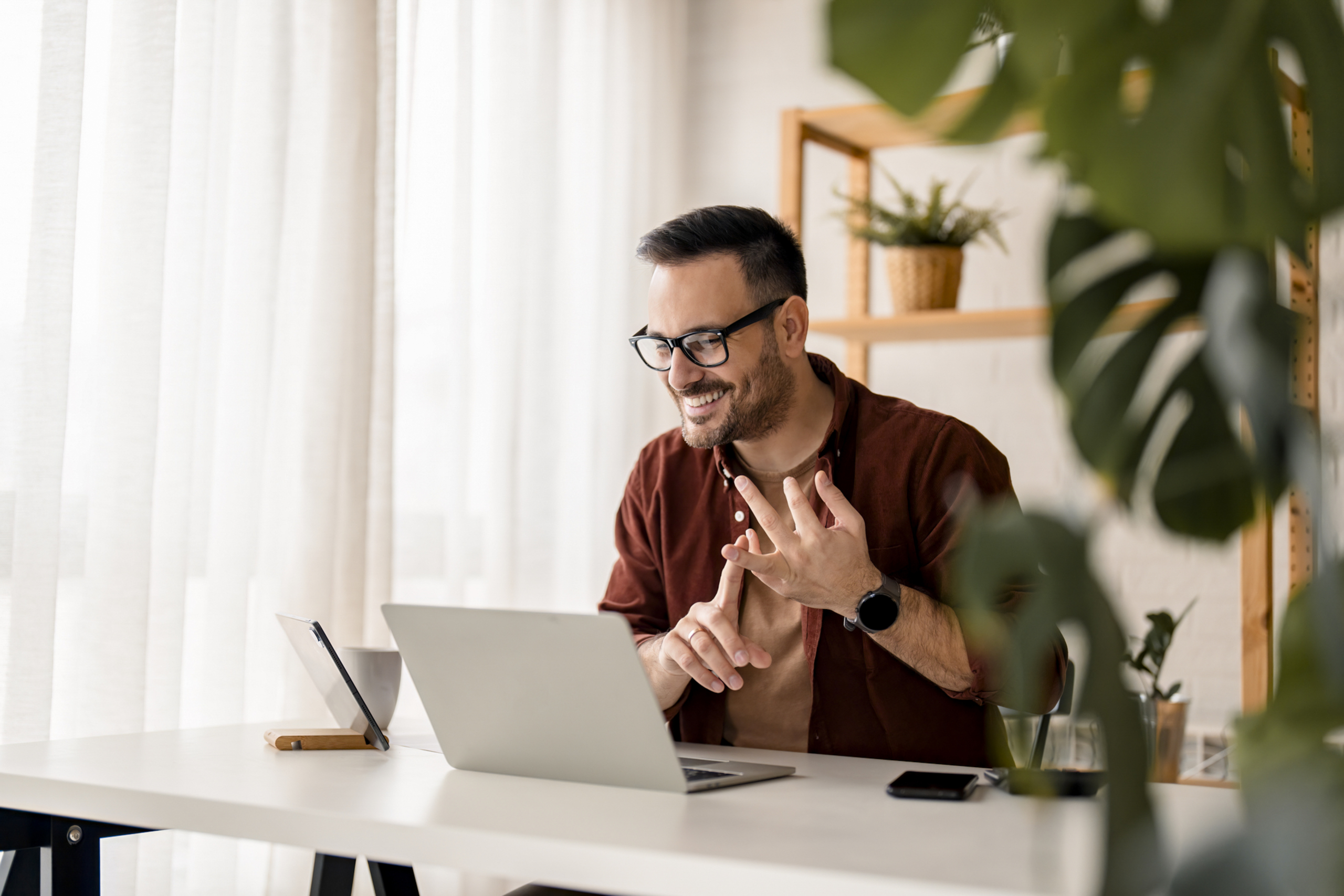 Cheerful young businessman employee gestures with hands during virtual video conference call in home office during the day.