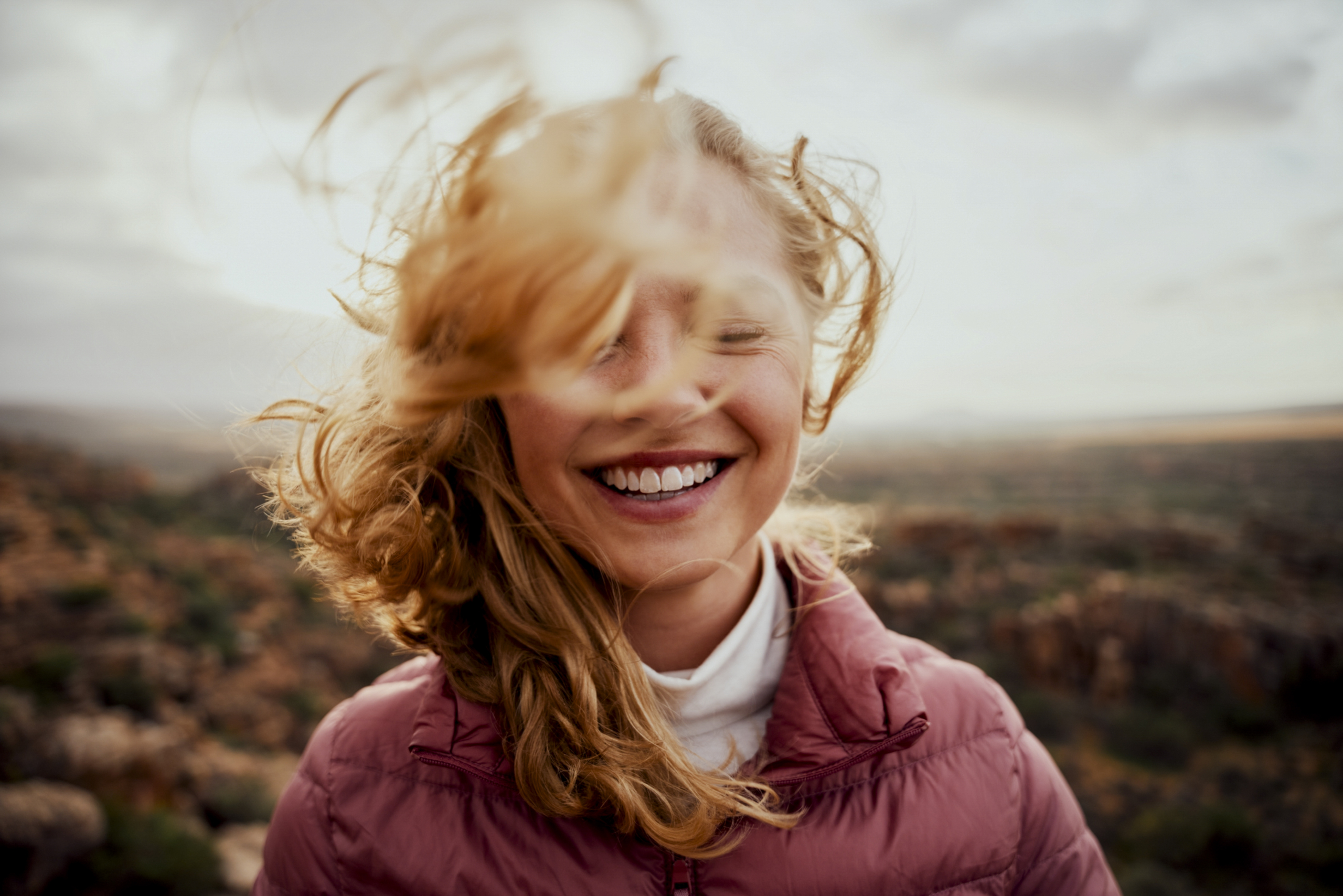 Outdoor portrait of young smiling woman. Her face is partially covered with flying hair