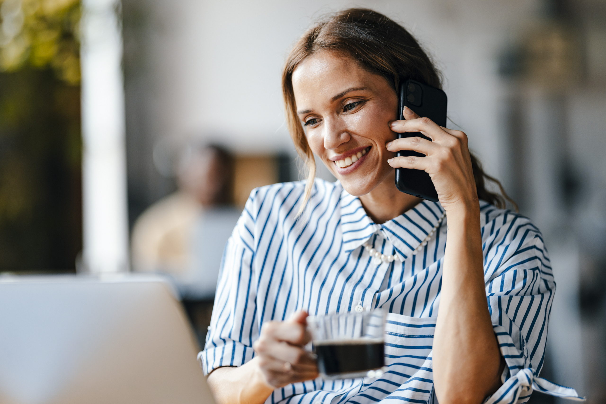 A smiling woman on the phone drinking coffee