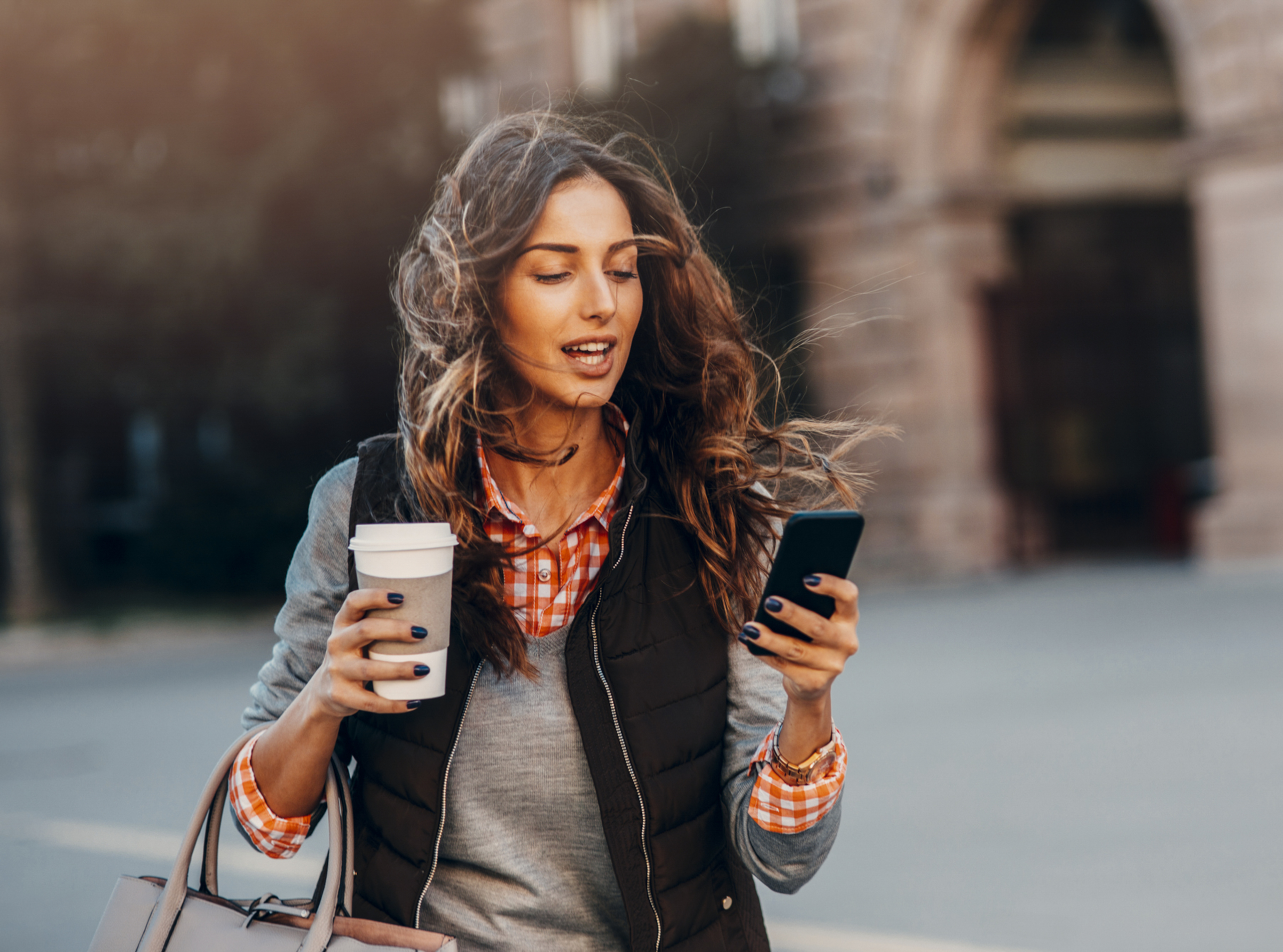A woman uses her phone on the go whilst drinking a take out coffee